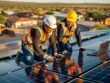Two tribal workers install solar panels on a rooftop at golden hour while one reviews coursework on an open laptop nearby.
