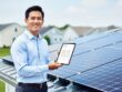 A solar energy sales representative stands beside rooftop solar panels while presenting information on a tablet, suggesting professional training for solar sales.